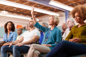 People sitting at event with one person raising his/her/their hand.